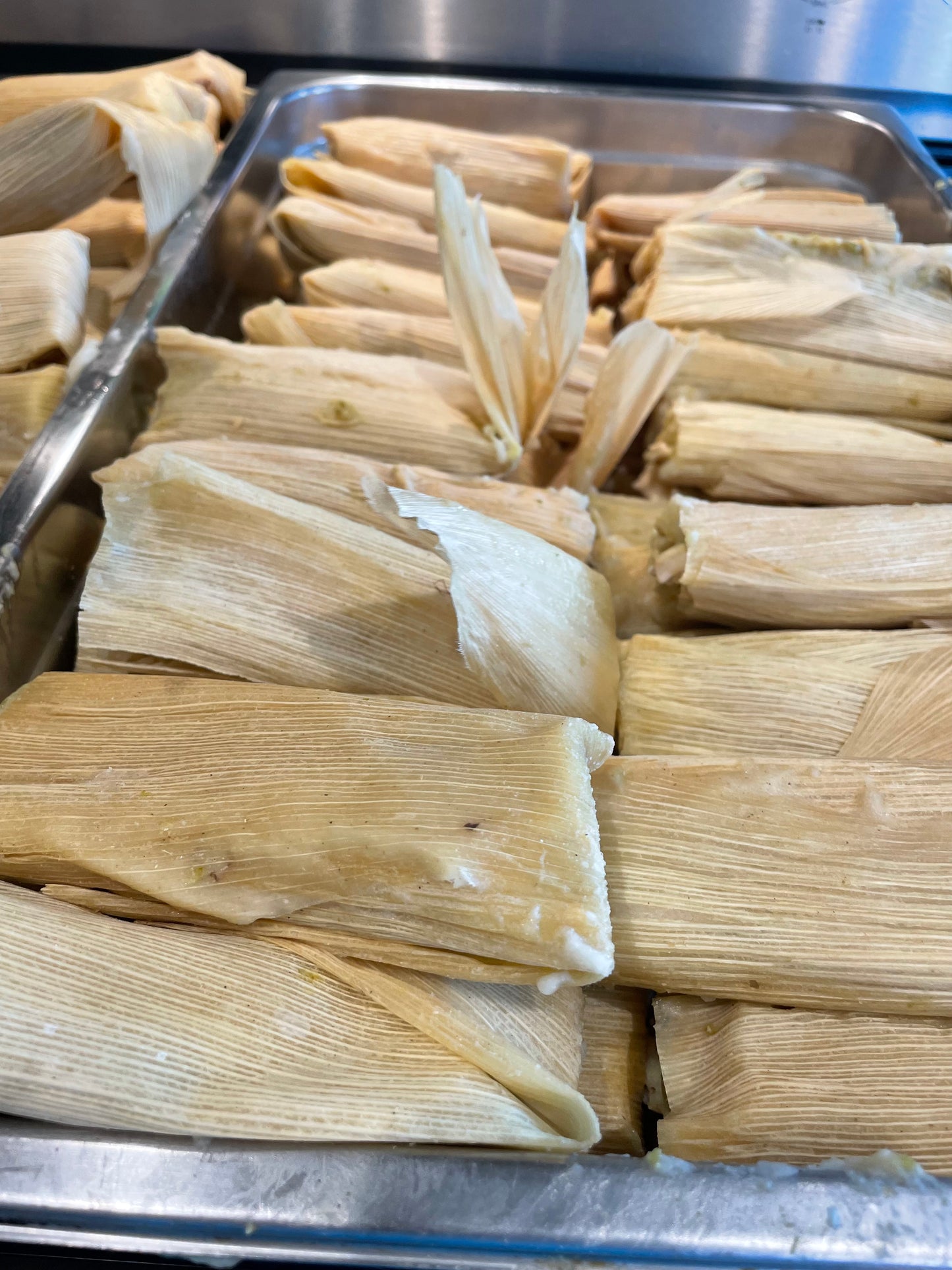 Stacks of green Chile tamales on a stainless steel trays.