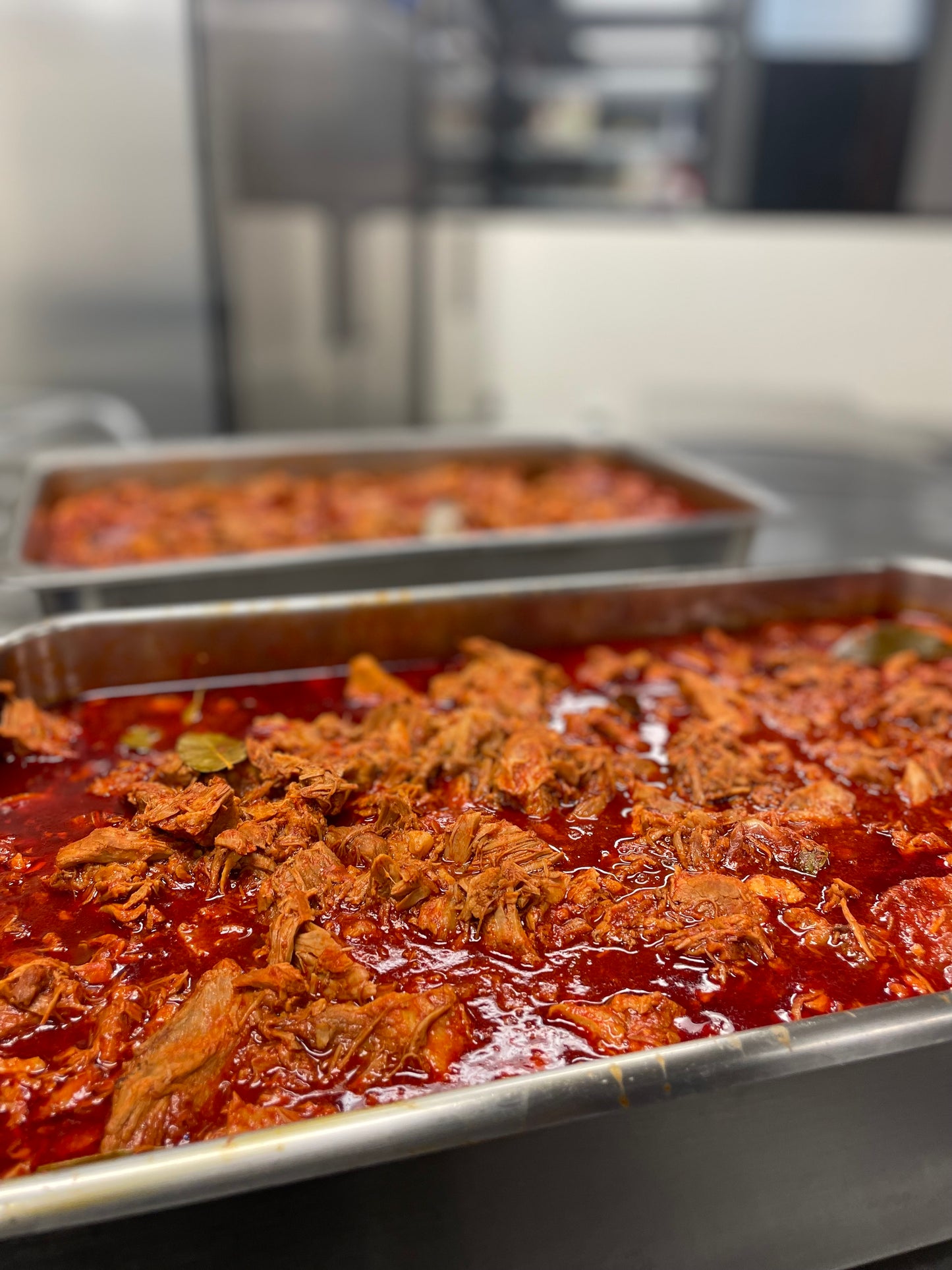 Tray of meat in a mild red Chile sauce in a kitchen setting