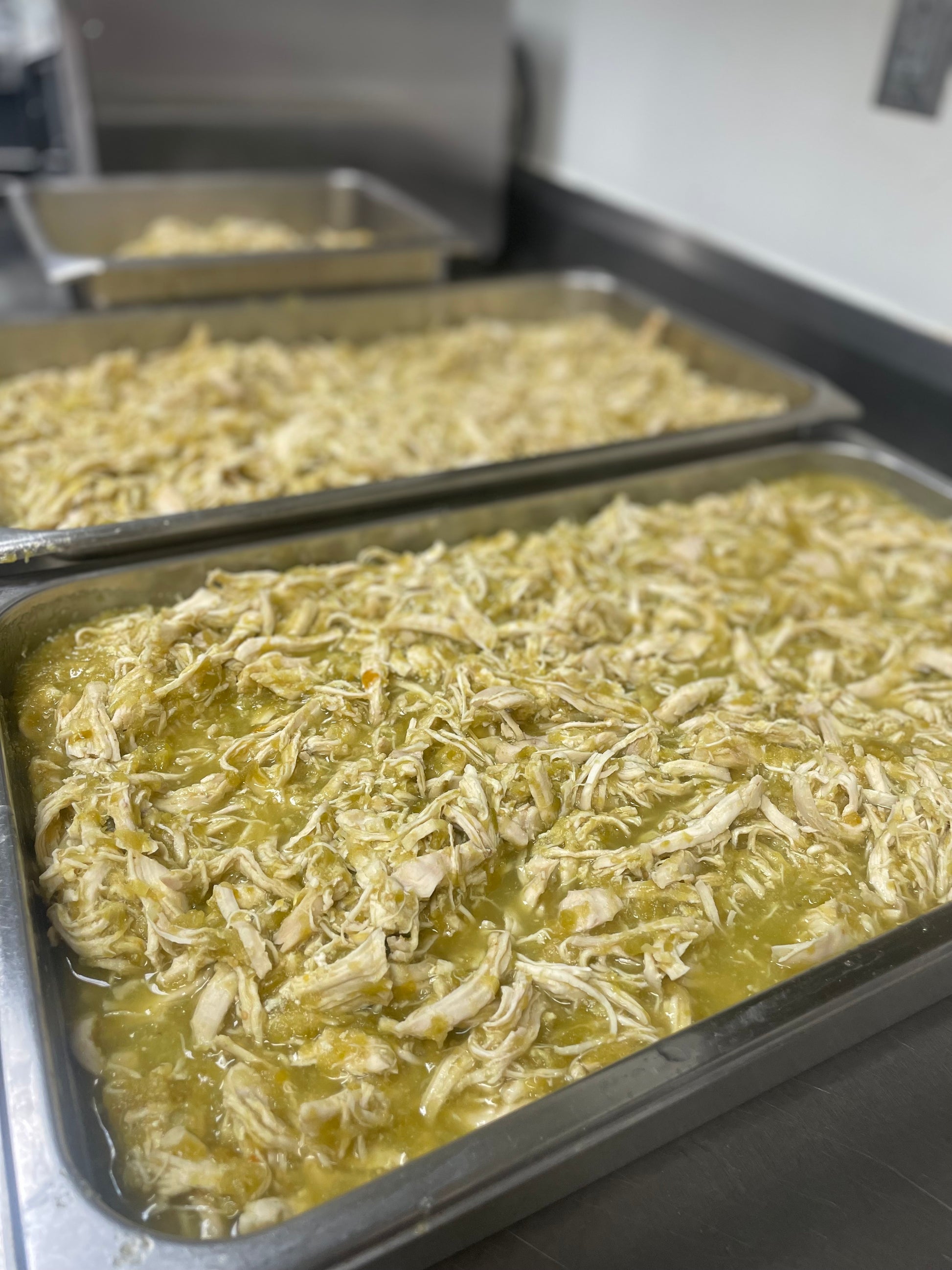 Two trays of shredded chicken in a kitchen setting