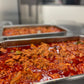 Tray of meat in a mild red Chile sauce in a kitchen setting